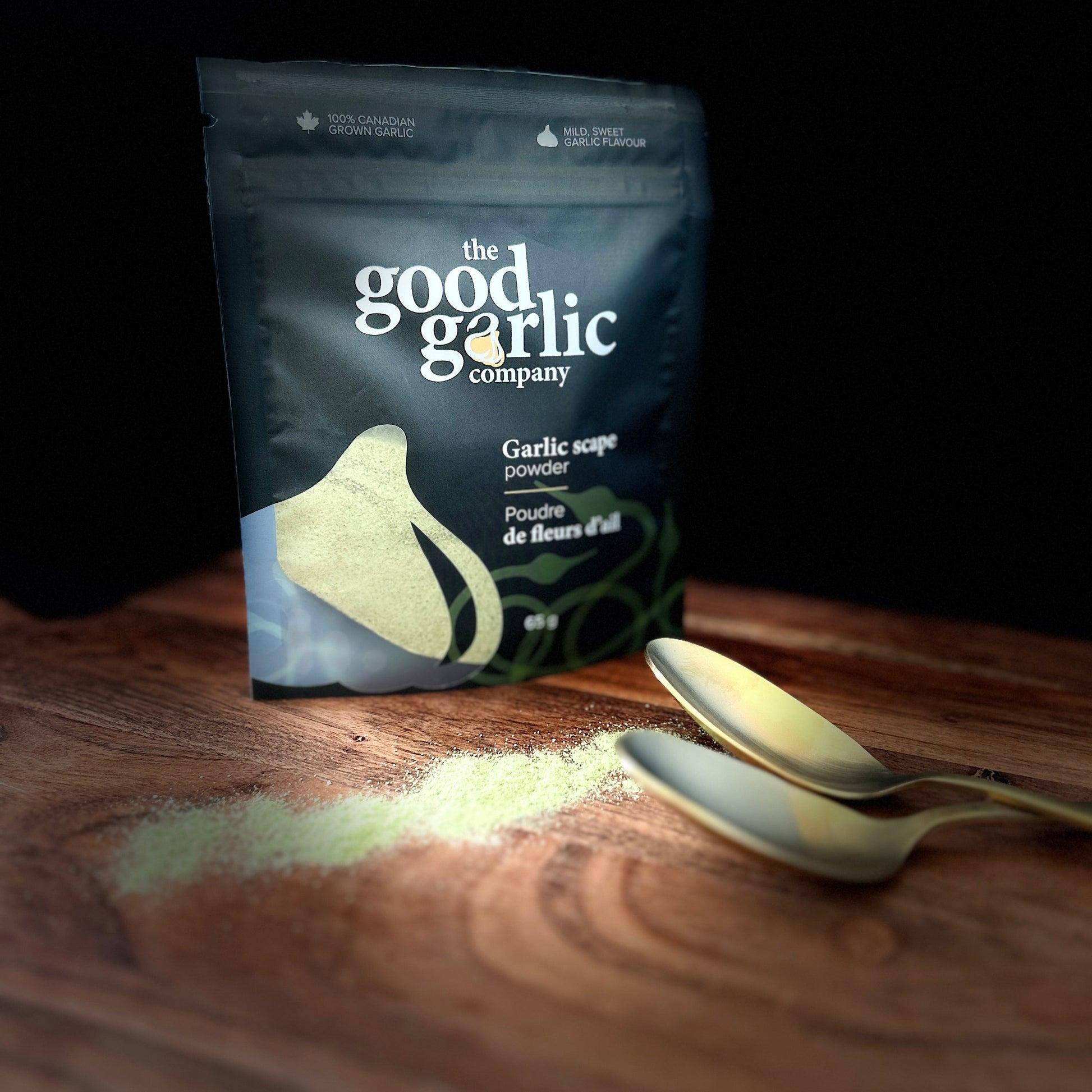 Packaging of 'the good garlic company' garlic powder on a wooden surface with a spoon.
