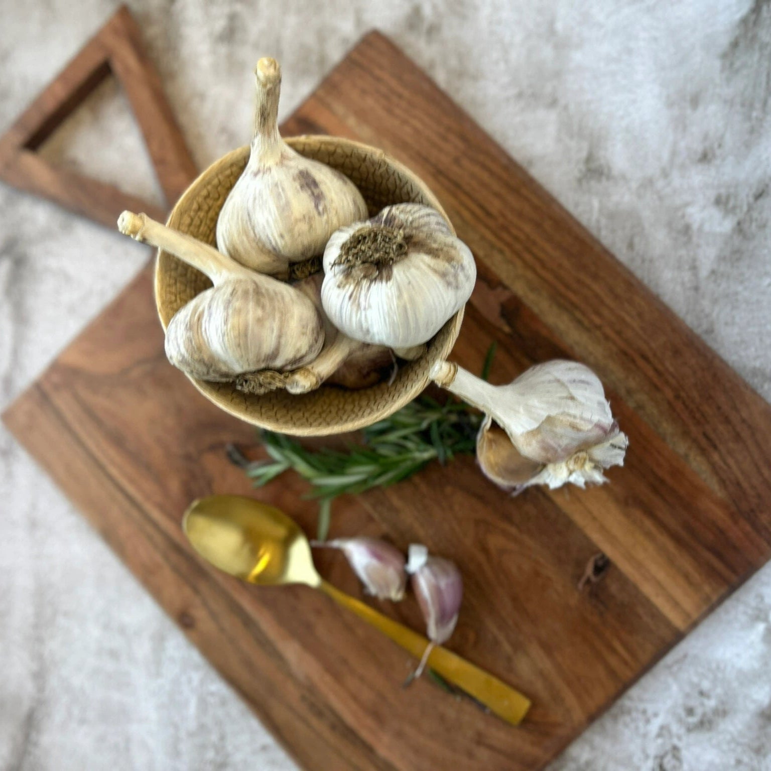 Garlic bulbs in a bowl on a wooden cutting board with a gold spoon