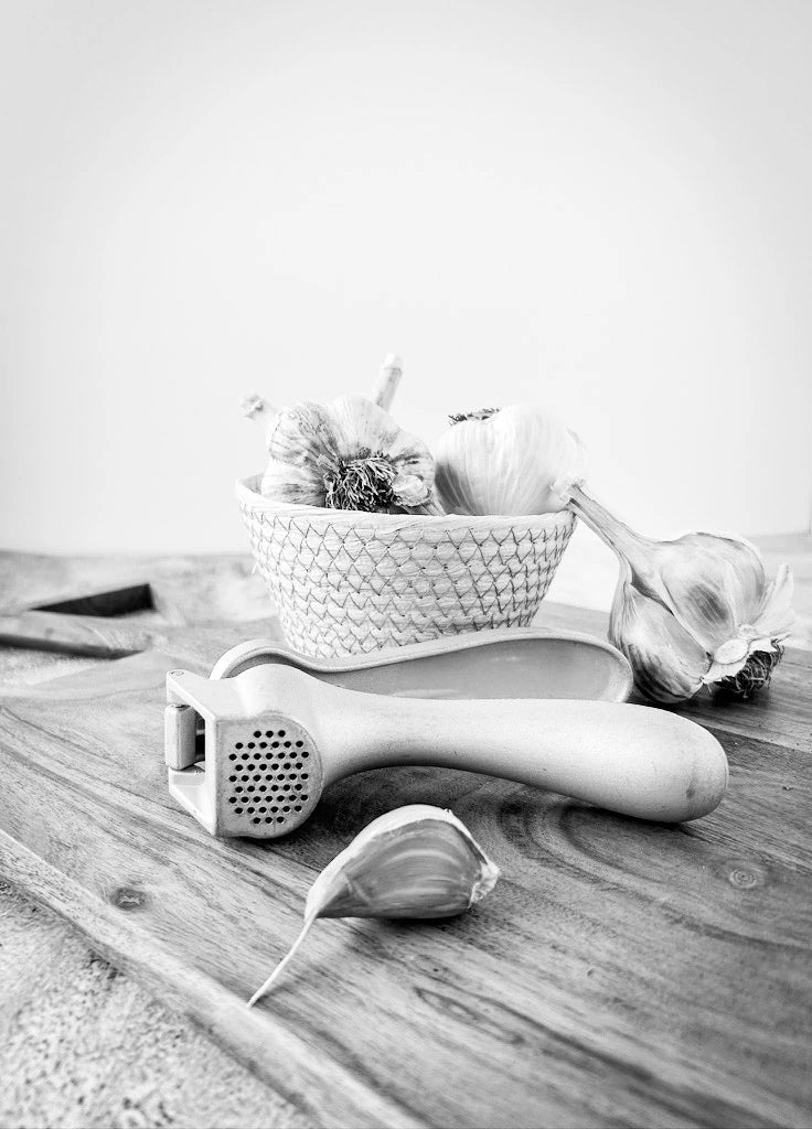 Garlic press and garlic cloves on a wooden surface with a white background