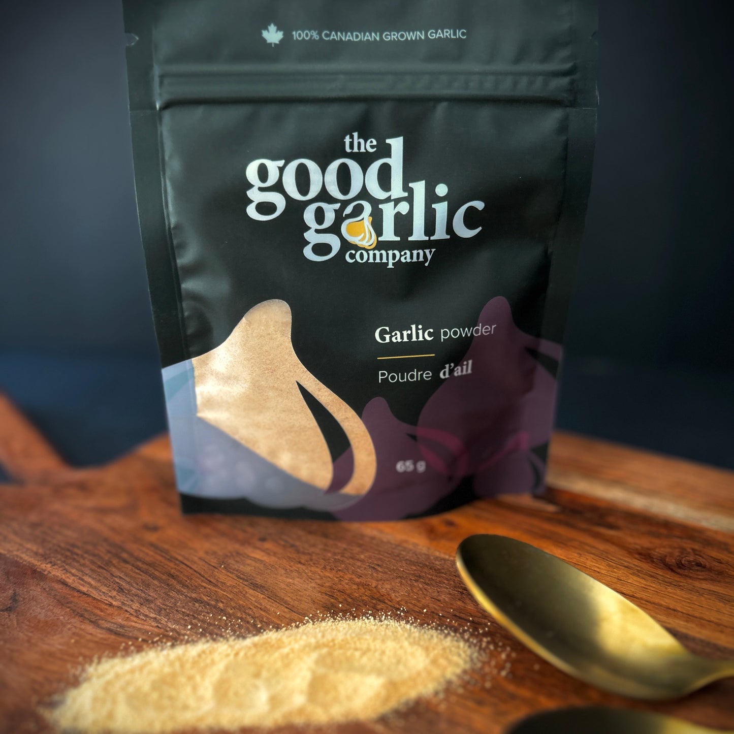 Good Garlic Company garlic powder package on a wooden surface with garlic powder and a spoon.